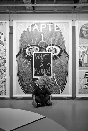 The artist Trenton Doyle Hancock sits in front of one of the panels at the show. Photo courtesy of Massachusetts Museum of Contemporary Art