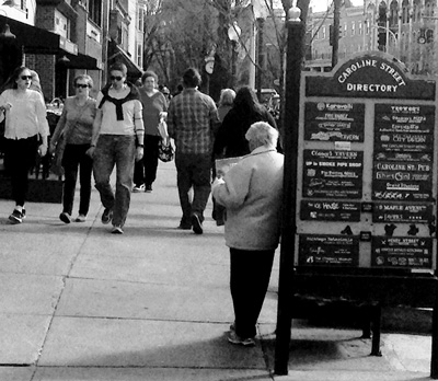 A panhandler, leaning against the signboard at right, seeks donations from pedestrians on Broadway in Saratoga Springs. The city is debating new limits on what officials say is “agressive panhandling.”Thomas Dimopoulos photo