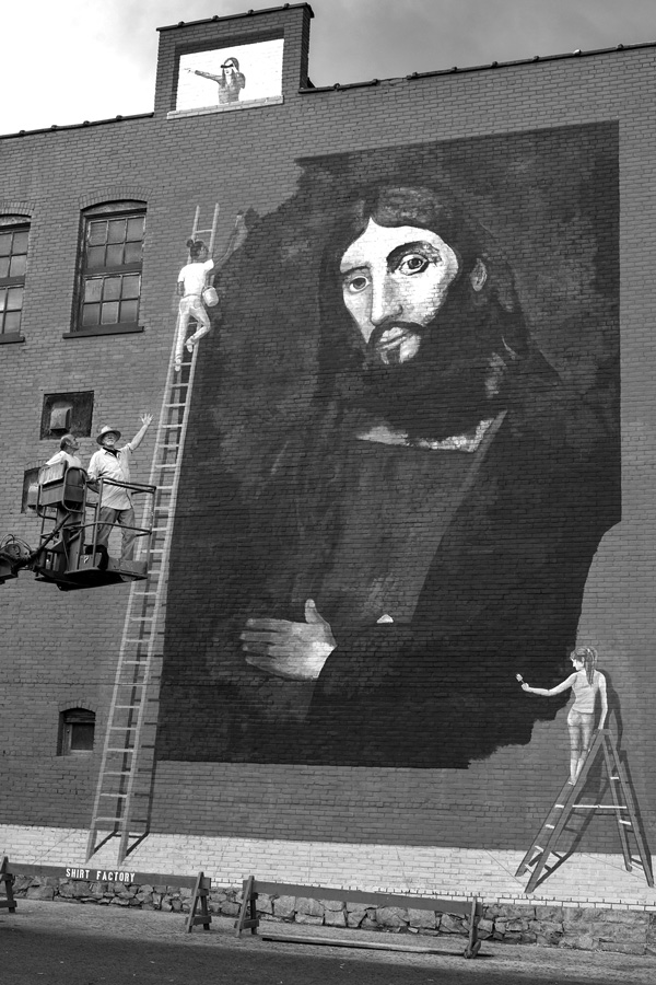 The Glens Falls artist Esmond Lyons gestures from a construction lift toward his new mural on the side of a building in the city’s east end. Joan K. Lentini photo