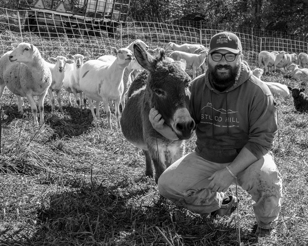Jesse McDougall kneels with Ben, a donkey whose job is to keep the sheep safe from predators at Studio Hill Farm in Shaftsbury, Vt. McDougall has worked to make the farm a model of regenerative agriculture. Joan K. Lentini photo